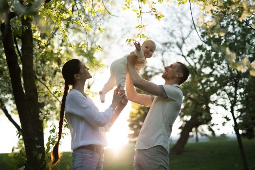 Happy man and woman playing with baby outdoors